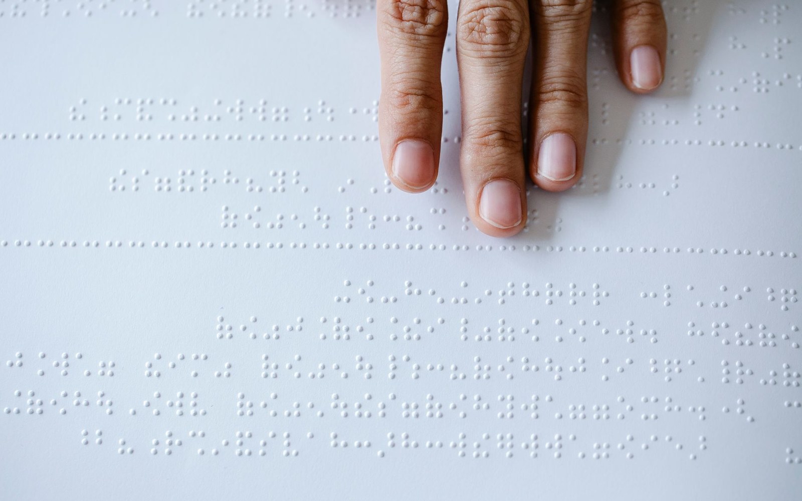 Fingers reading rows of raised braille dots on a white page